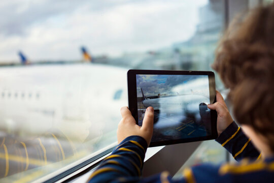 Young boy taking pictures of a airplane on a tablet in the airport