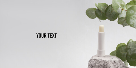 White tube of hygienic lipstick on a stone with a sprig of eucalyptus. Beauty minimal still life....
