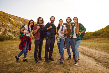 Portrait of a happy smiling joyful group of friends tourists standing outdoor having walking tour of the mountains and looking cheerful at the camera. Hiking, adventure and people travel concept.