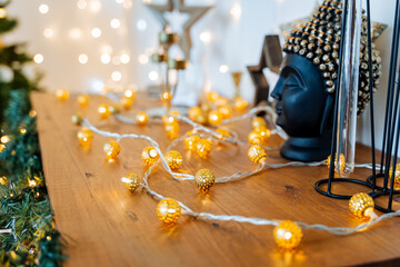 A glowing garland lies on the table, round yellow lights, a Buddha head, a black statuette, a festive New Year's background, an atmosphere of fun, miracles.