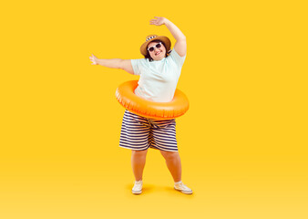 Full body photo of a happy funny fat plus size overweight woman in sunglasses with rubber ring and hands up isolated on studio yellow background. Summer holiday trip and vacation concept.