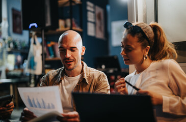 Confident colleagues strategize project details in a bustling coffee bar. Together, they review paperwork for profitable opportunities. Remote teamwork ensures successful planning.