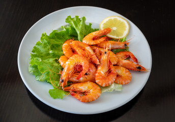 Mediterranean seafood dish of boiled shrimp on a plate in greens with lemon. On a black background.