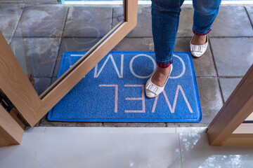Woman standing on mat with word Welcome on cement floor. Overhead view of welcome mat outside...