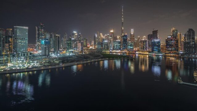 Panorama showing aerial view to Dubai Business Bay and Downtown with the various skyscrapers and towers along waterfront on canal night timelapse. Construction site with cranes