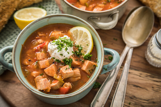 Ost Deutsche DDR GDR Soljanka Eintopf Suppe mit Jagdwurst, Saure Gurken, Letscho, Schmand, Zitrone, Toast und Petersilie auf Holzbrett mit L&ouml;ffel, Salzstreuer und hell grau Stein Hintergrund