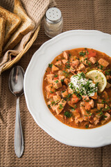 Ost Deutsche DDR GDR Soljanka Eintopf Suppe mit Jagdwurst, Saure Gurken, Letscho, Schmand, Zitrone, Toast und Petersilie mit Löffel, Salzstreuer und braun Stoff Hintergrund