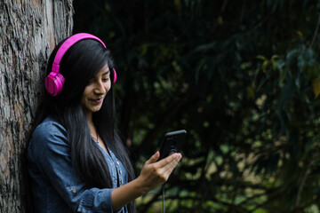 Mujer joven atractiva con auriculares disfrutando de música o un podcast en el parque o bosque,...