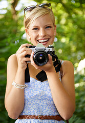 Portrait, camera lens and photographer with woman in forest for smile, memory and photography. Summer, happy and adventure with person and shooting for vacation, holiday and environmental tourism