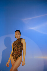 Young woman in bodysuit posing against blue background.