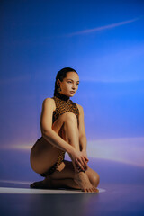 Young woman in bodysuit posing barefoot against blue background.