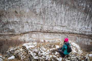 Girl sitting high on a rock in the mountains looking down, admiring nature, mountain trip alone,...