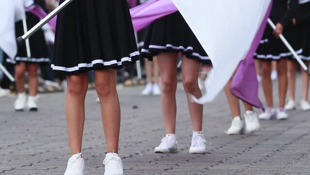 Group of cheerleaders wearing short brown skirt waving flags during a parade, close up legs