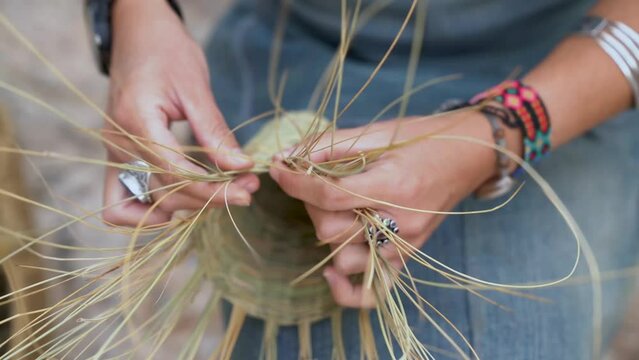 Front view of Hispanic woman weaving a basket with esparto fibers. Manual work, tradition and culture. Close up.