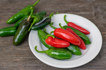 Capsicum annuum Jalapeno chilli hot peppers, group of green and red fruits on wooden brown table on white plate