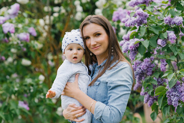 Young happy mother holds a cute little son in her arms. Happy family playing and cuddling in the park