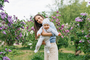 Happy European mother lifts up her little smiling son in her arms in the spring on a walk in the park