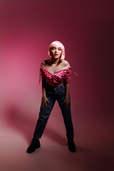 Stylish woman with pale pink hair wearing a pink jacket and jeans poses confidently against a pink background. Fashion advertising concept, individuality and confidence.
