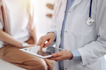 Doctor and patient in clinic. Friendly physician using tablet computer near a young woman. Medicine concept