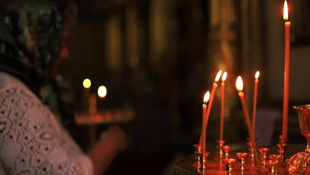 burning candles in a temple or church in the dark standing in a candlestick against the background of a woman who crosses herself and prays