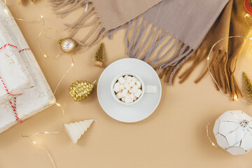 Cup of coffee, gift box and knitted sweaters, led lights on beige background. Hygge style, winter...