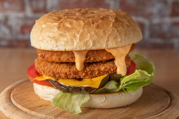 smoked chickenburger with aubergine, salad, tomato, and sauce centred on wooden plate on dim wall background with bricks 