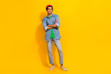 Fototapeta na wymiar Full length photo of cute young male folded arm look empty space dressed stylish jeans garment isolated on yellow color background