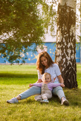 Obraz premium Mother plays with cute blonde baby toddler in the park at sunset. The concept of a happy childhood, a strong family. Sun rays with selective focus
