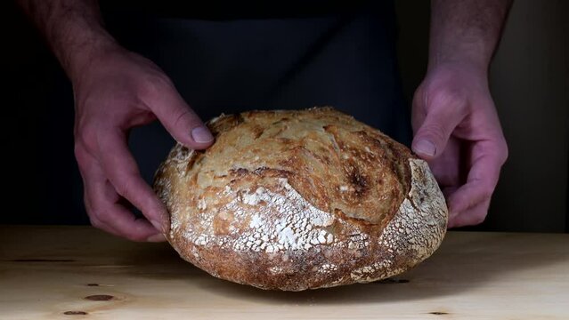 Young man's hands leaving a crusty sourdough bread on a table.