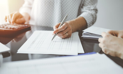 Woman accountant using a calculator and laptop computer while counting taxes for a client. Business audit and finance concepts