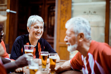 Senior sports fans sharing a laugh over beers at a street cafe