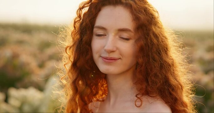 Portrait of beautiful woman with red curly hair looking at camera, smiling.