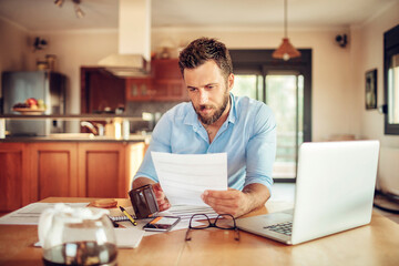 Concerned young man reading through bank statements at home