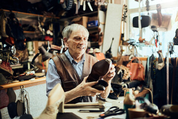 Elderly craftsman inspecting a handcrafted shoe in his traditional workshop