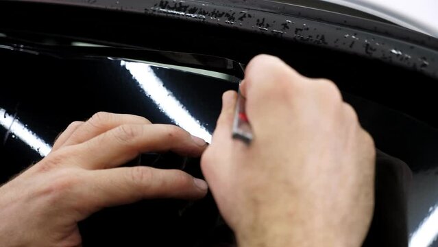 The car mechanic cuts off the excess tinting foil when gluing on the car glass in the garage. Installing car window tint.