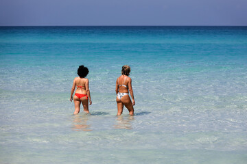 Two women in bikini going to swim in sea water, rear view. Girlfriends on a beach, vacation concept