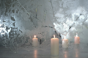 Holiday decoration with four white candles in front and behind frozen glass and a few bare branches...
