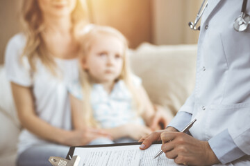 Obraz premium Doctor and patient. Pediatrician using clipboard while examining little girl with her mother at home. Sick and unhappy child at medical exam