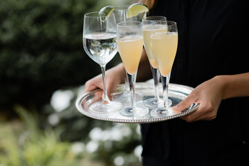closeup of server's hands holding silver tray of water garnished with lime wedges and bellini cocktails
