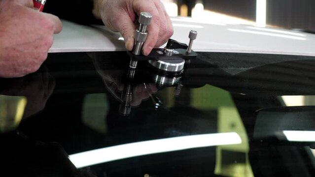 Specialist repairs dangerous crack in windshield on location without replacement glass for free. Mechanic using repairing equipment to fix damaged windshield.