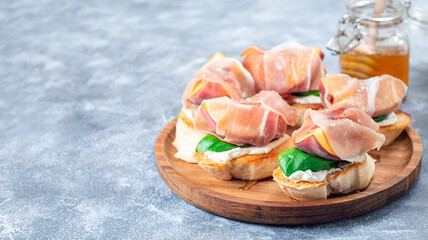 Prosciutto peach bruschetta on wooden plate, horizontal, copy space
