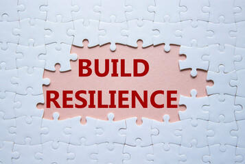 Build resilience symbol. White puzzle with words Build resilience. Beautiful pink background....