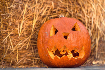Halloween. Pumpkin with a carved scary face, standing on hay in the sunlight