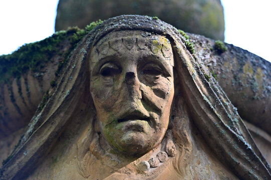 Partial view to a creepy sandstone sculpture which shows a noseless, female face.  