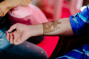 Mehndi master drawing henna tattoo on female