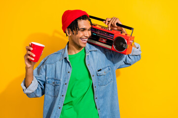Photo of positive cool meloman wear stylish denim jacket hold radio on shoulders drink cocktail isolated on vivid yellow color background