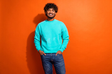 Photo of cheerful confident young man put hands pockets posing empty space isolated on orange color background