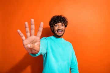 Photo funky indian young guy wearing cyan sweatshirt showing only four fingers surprised products left isolated on orange color background