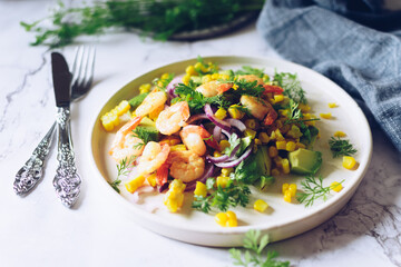 Healthy salad with fresh vegetables - corn, avocado, red onion, shrimp and coriander on a white plate.