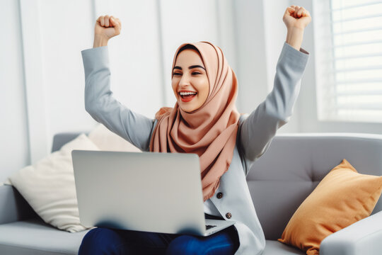 Beautiful middle age arab woman smiling and rejoicing after success. Happy woman celebrating business success on sofa in living room with computer.